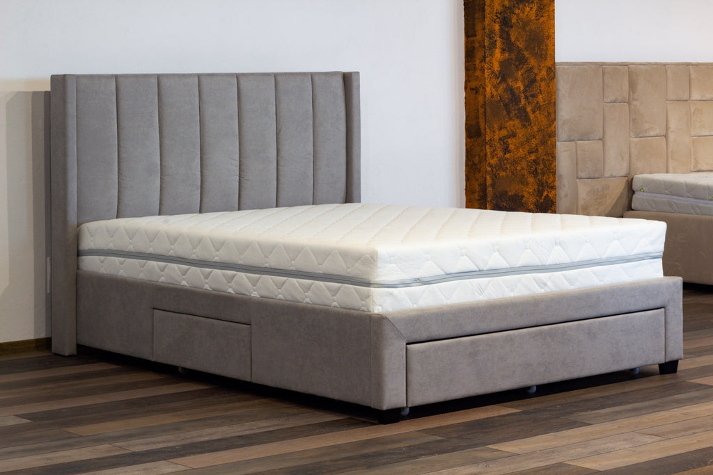 Gray upholstered bed with a quilted mattress on a wooden floor.