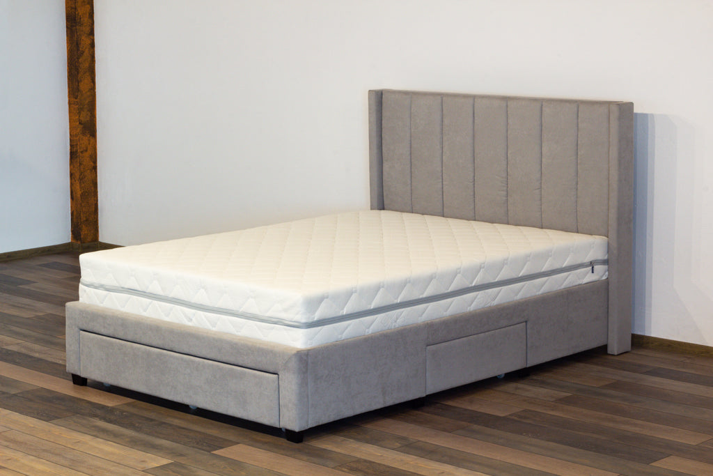 Gray upholstered bed with wooden headboard on a wooden floor.