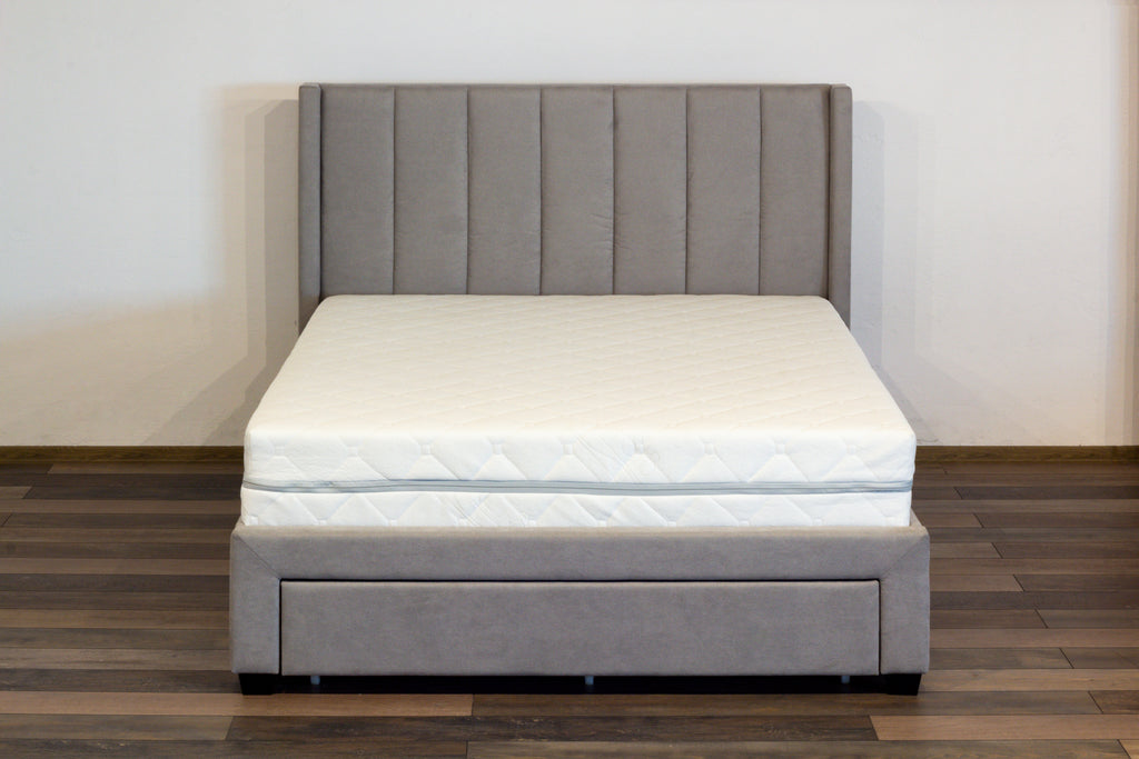 Gray upholstered bed with a white mattress on a wooden floor.