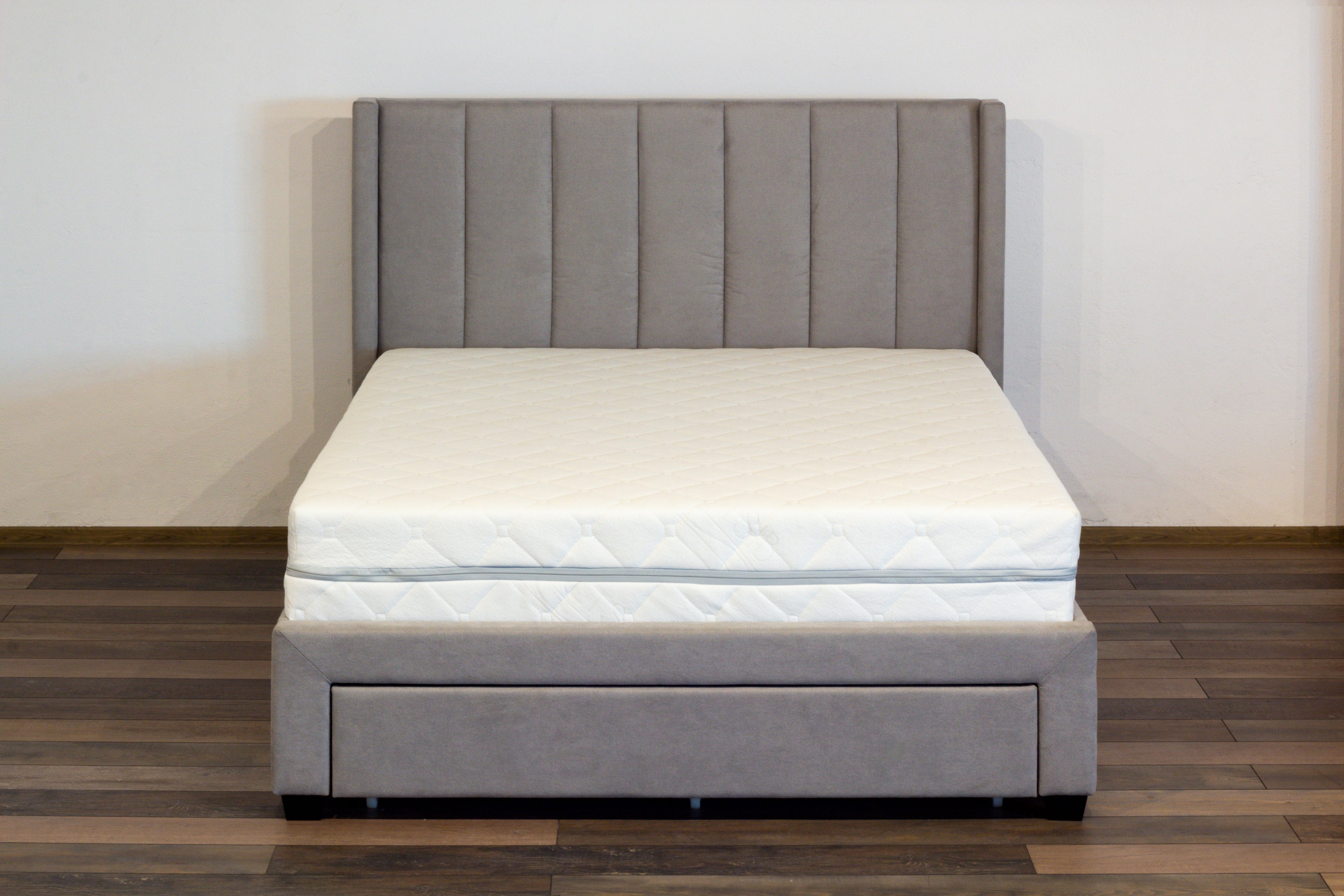 Gray upholstered bed with a white mattress on a wooden floor.