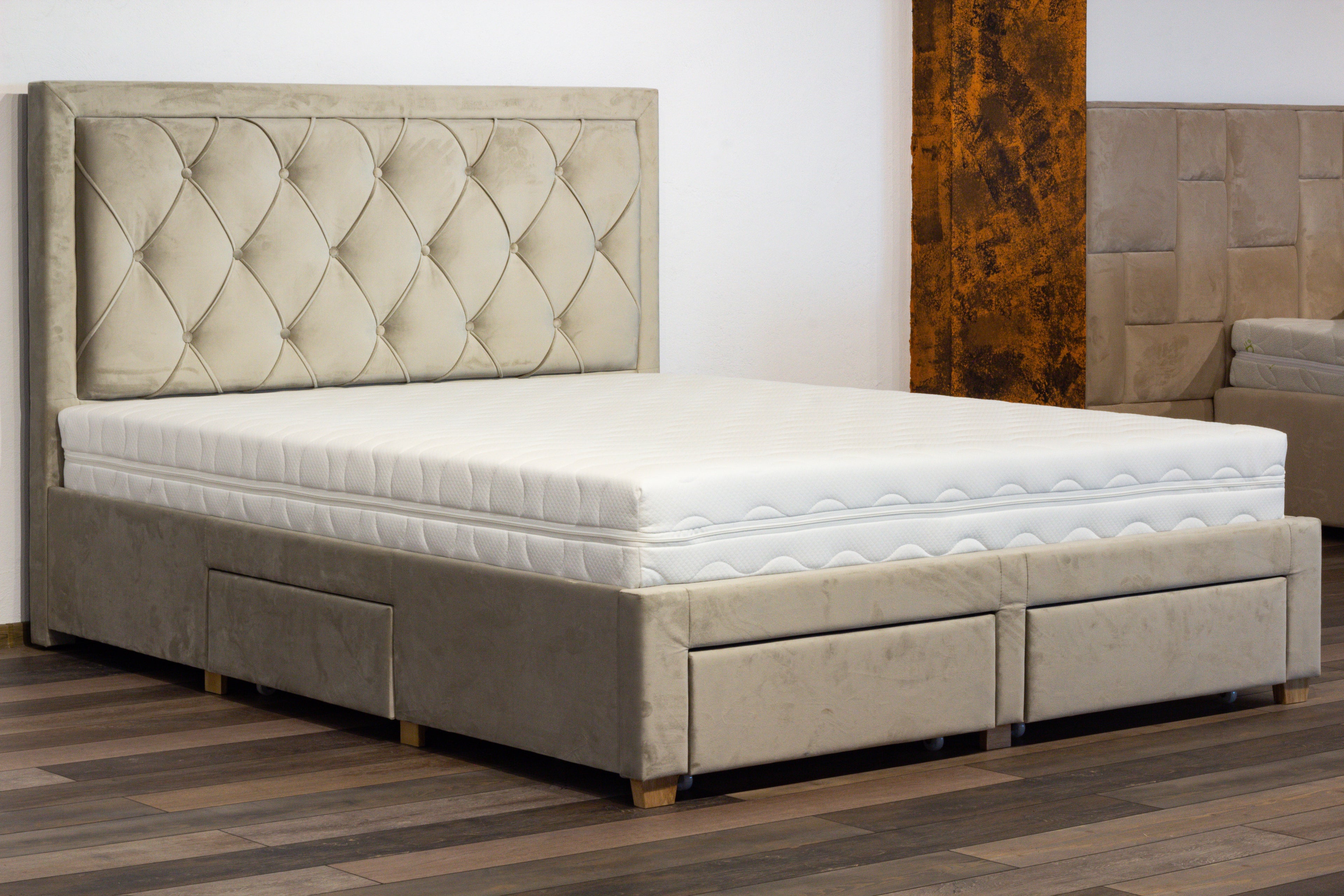 Beige upholstered bed with tufted headboard and storage drawers on a wooden floor.