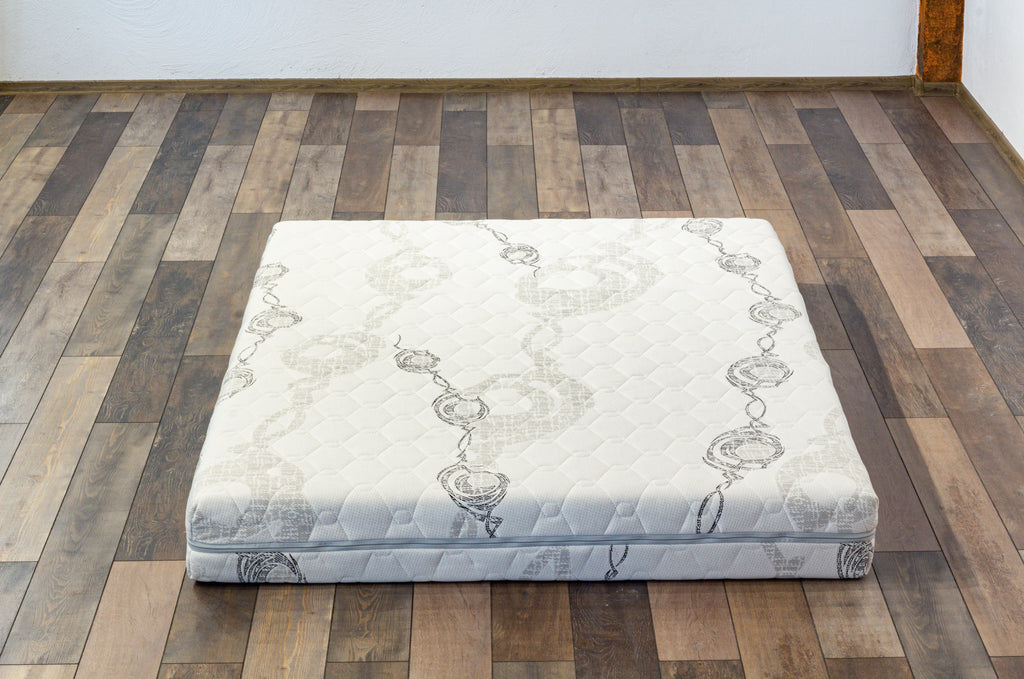 Mattress on a wooden floor with a plain wall background