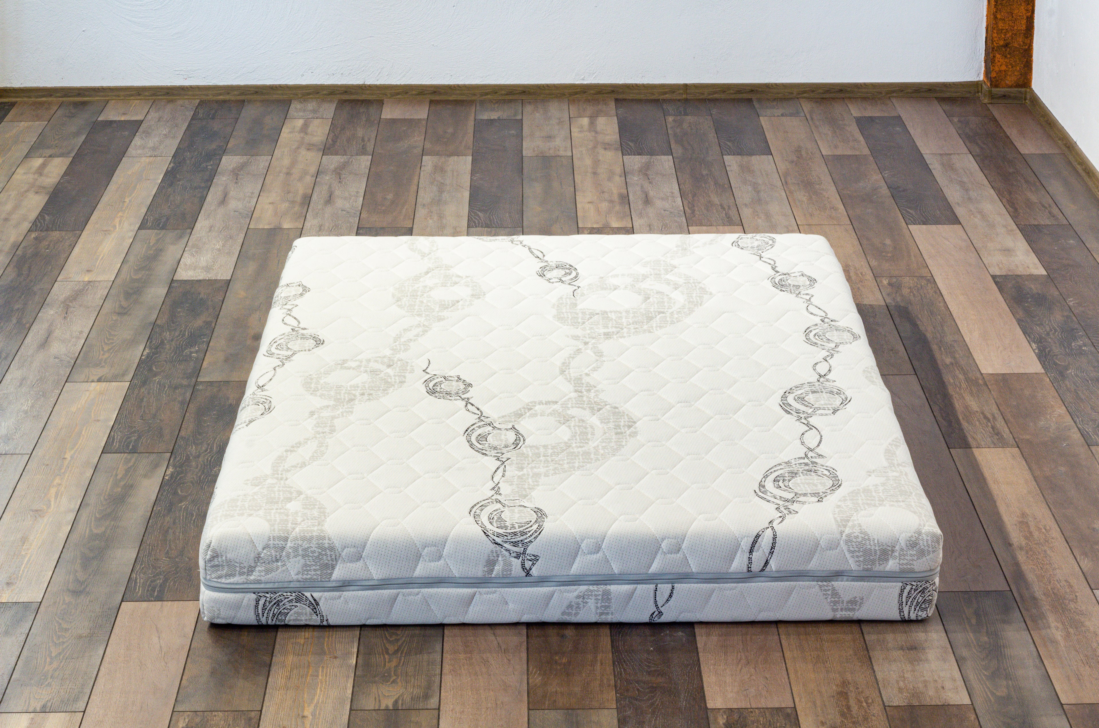 Mattress on a wooden floor with a plain wall background