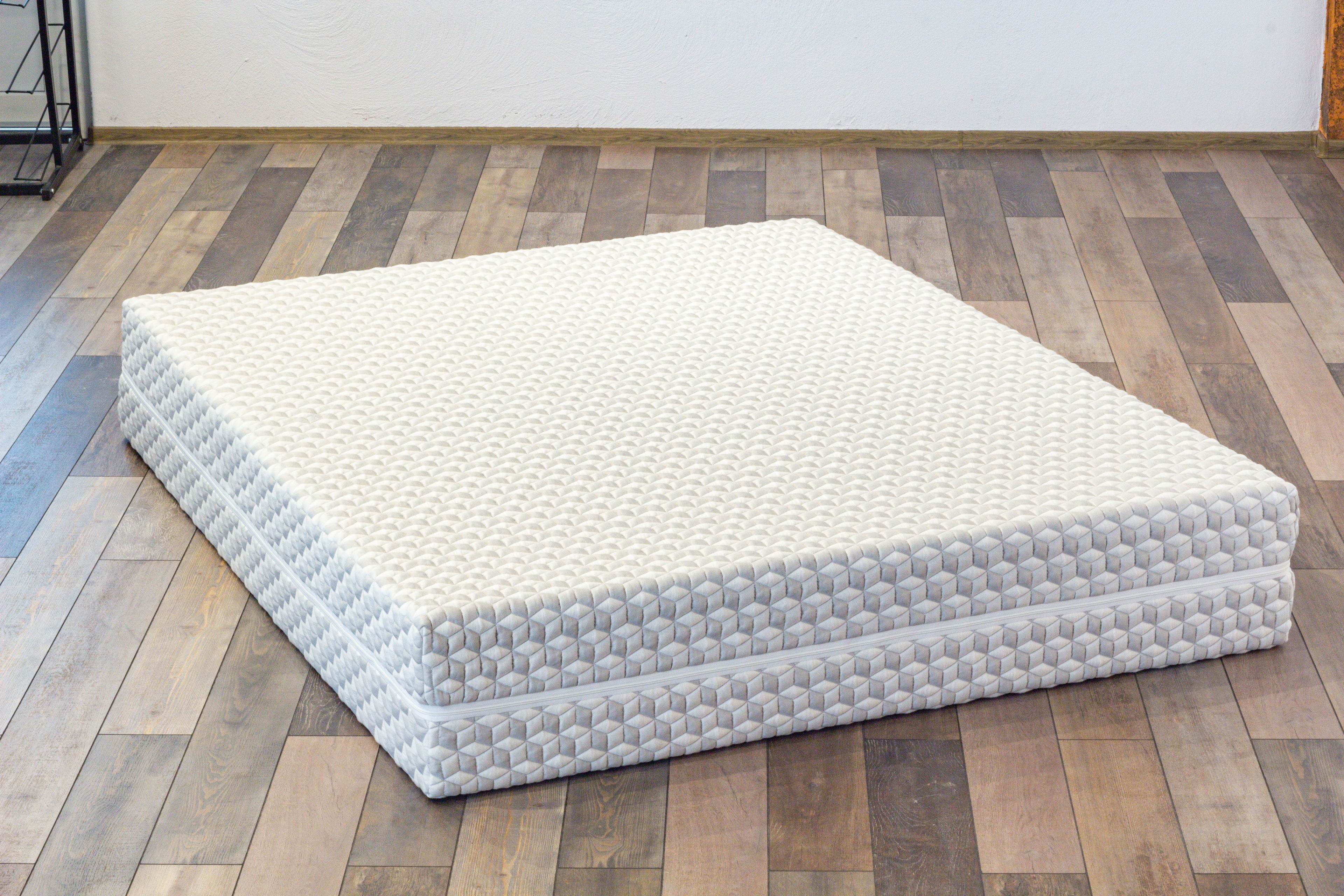 Mattress on a wooden floor with a white wall background