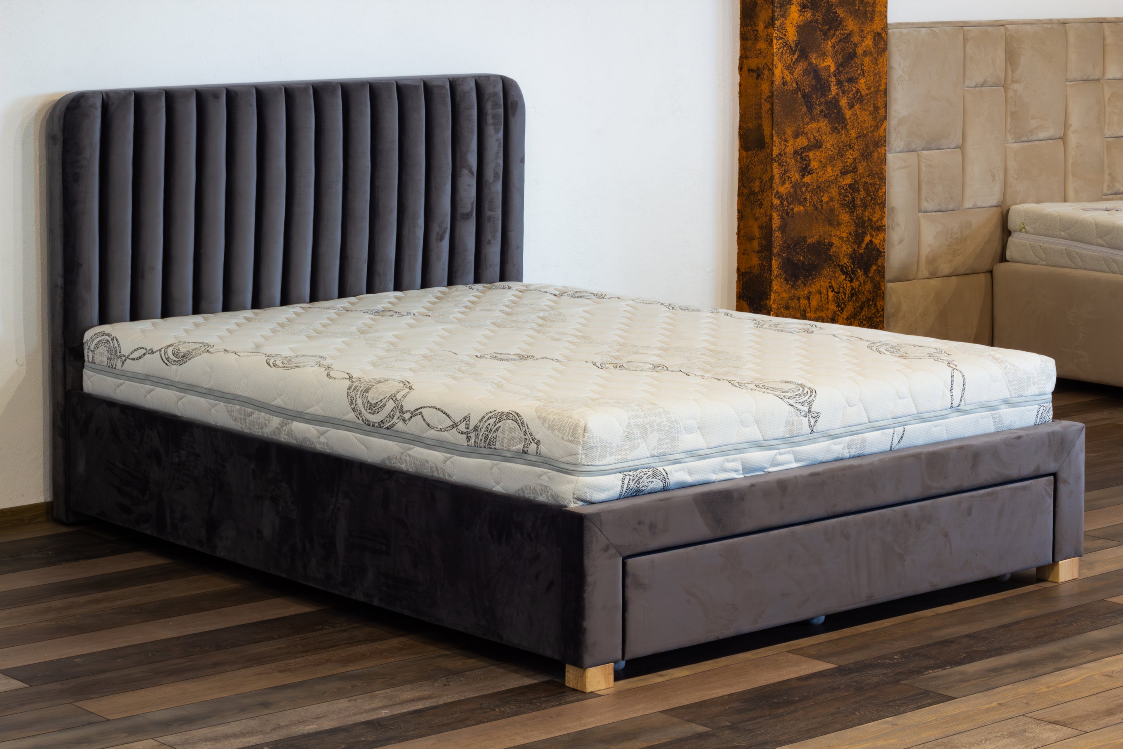 Gray upholstered bed with a mattress on a wooden floor.