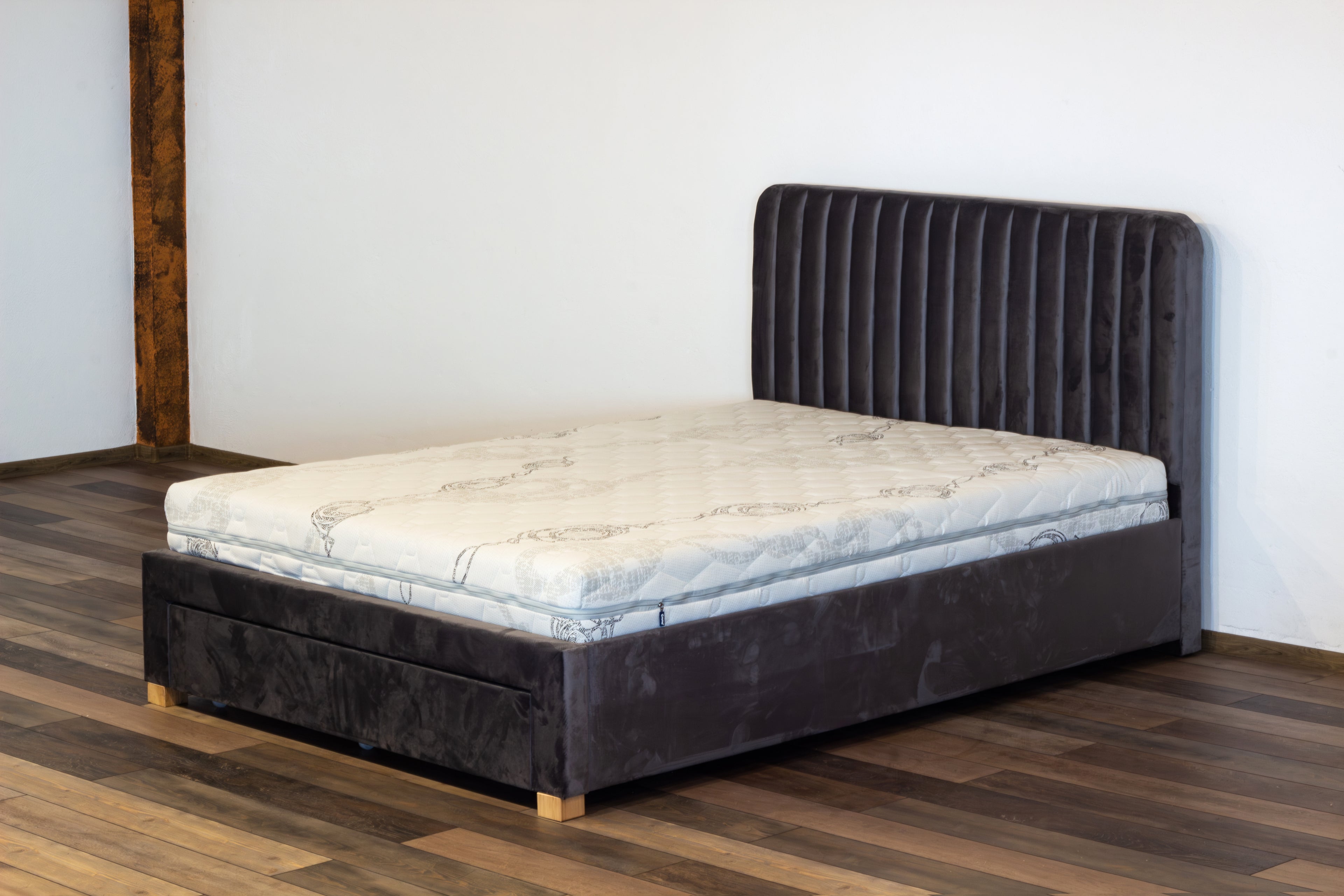 Dark upholstered bed with mattress on a wooden floor