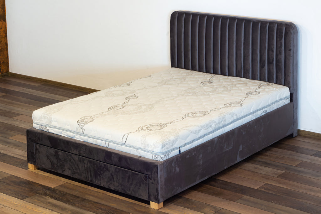 Bed with a gray upholstered headboard on a wooden floor.