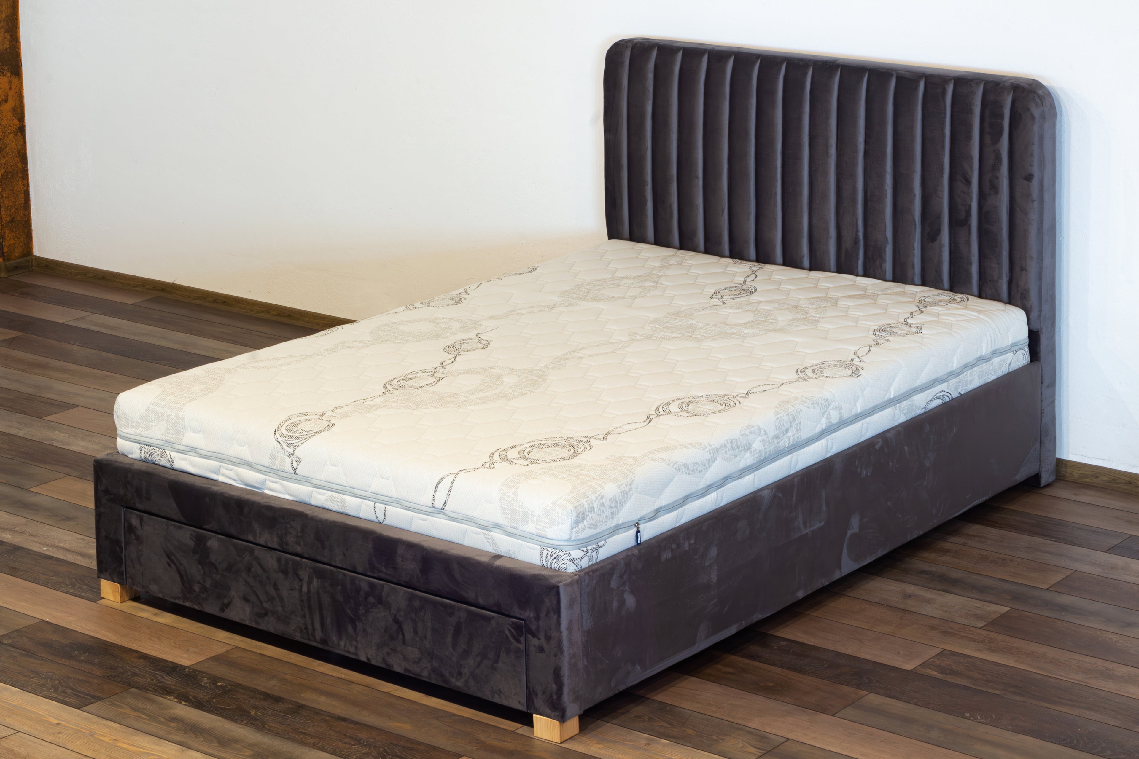Bed with a gray upholstered headboard on a wooden floor.