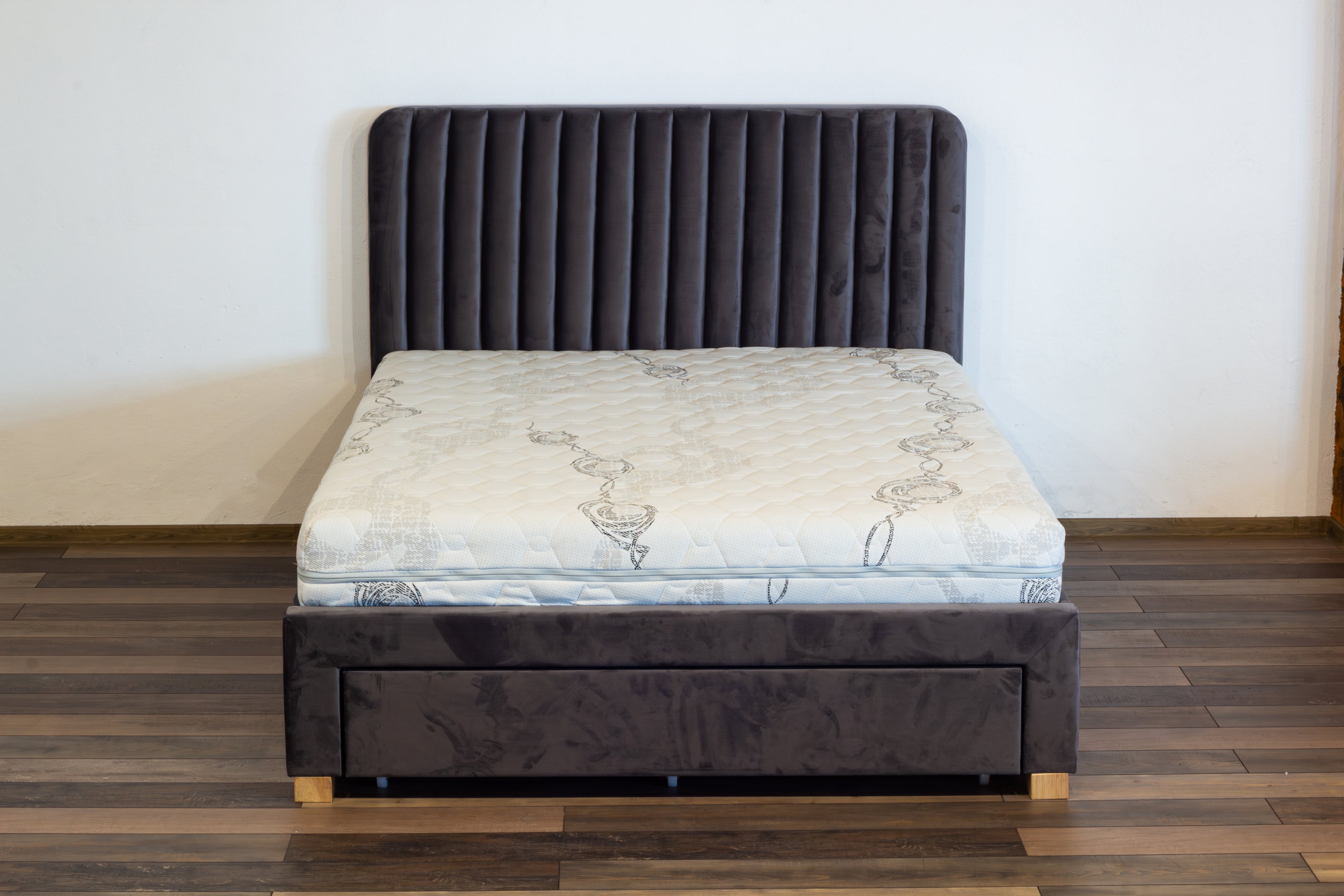 Gray upholstered bed with a mattress on a wooden floor.