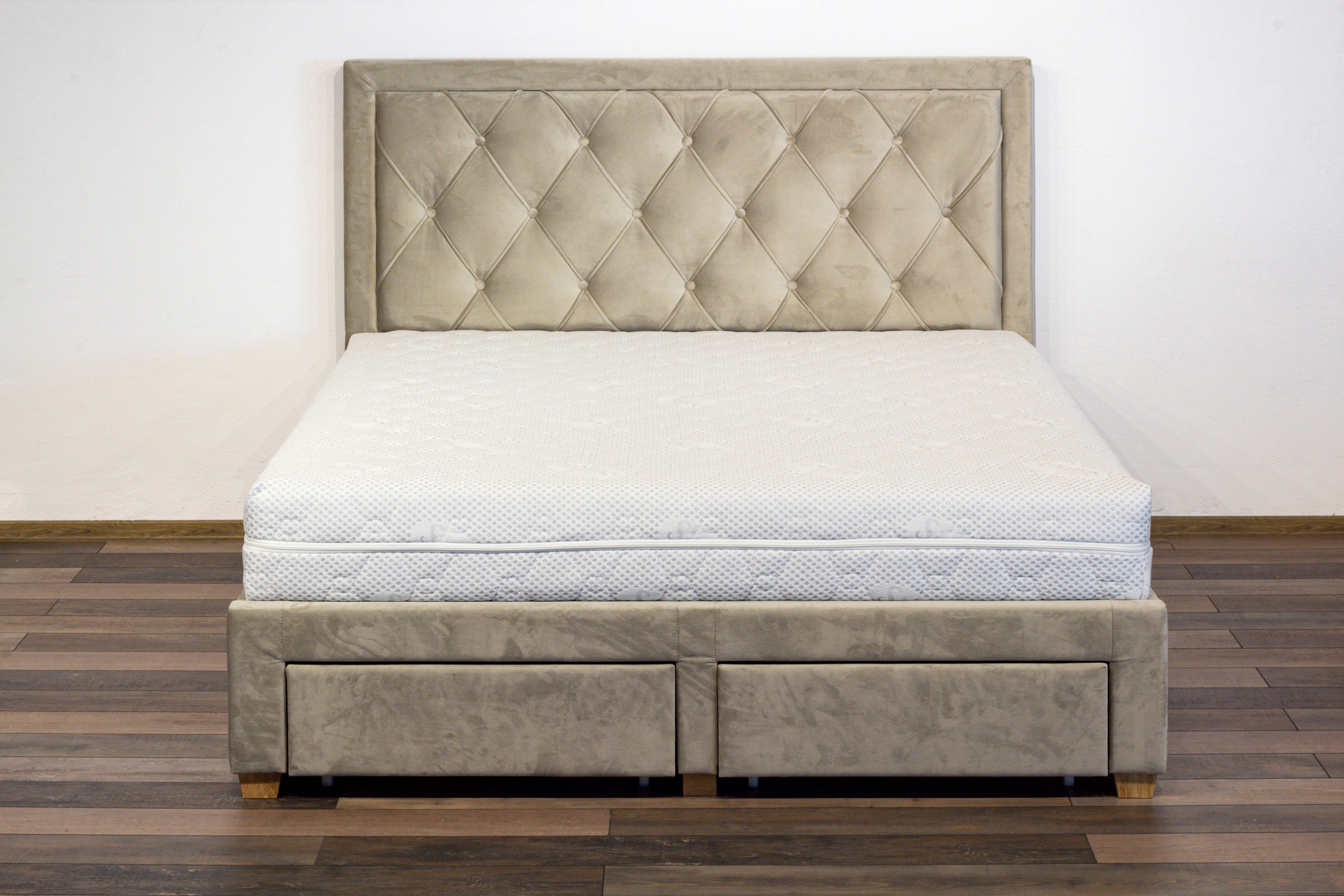 Beige tufted bed with mattress on a wooden floor