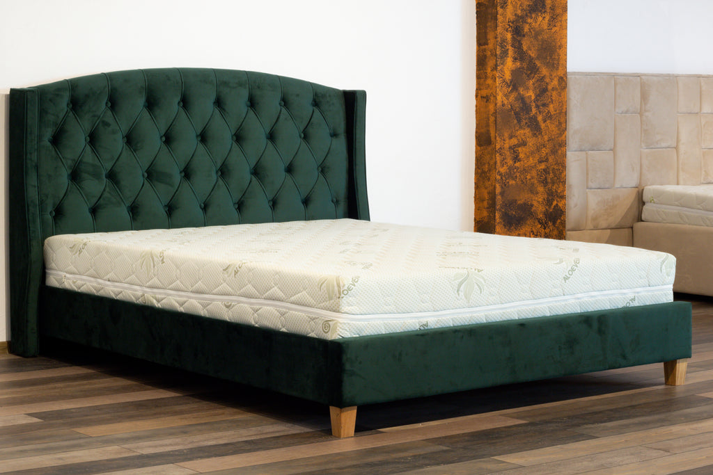 Green tufted bed frame with white mattress in a room setting.