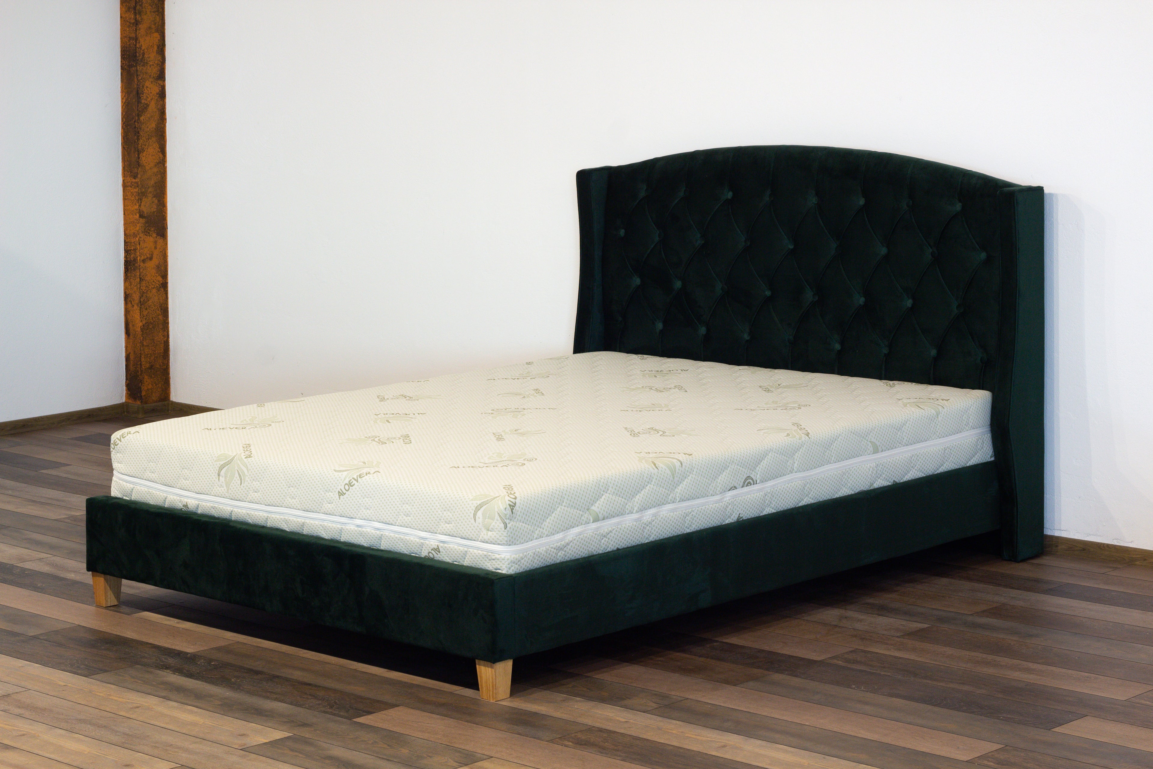 Dark green bed frame with white mattress on a wooden floor.
