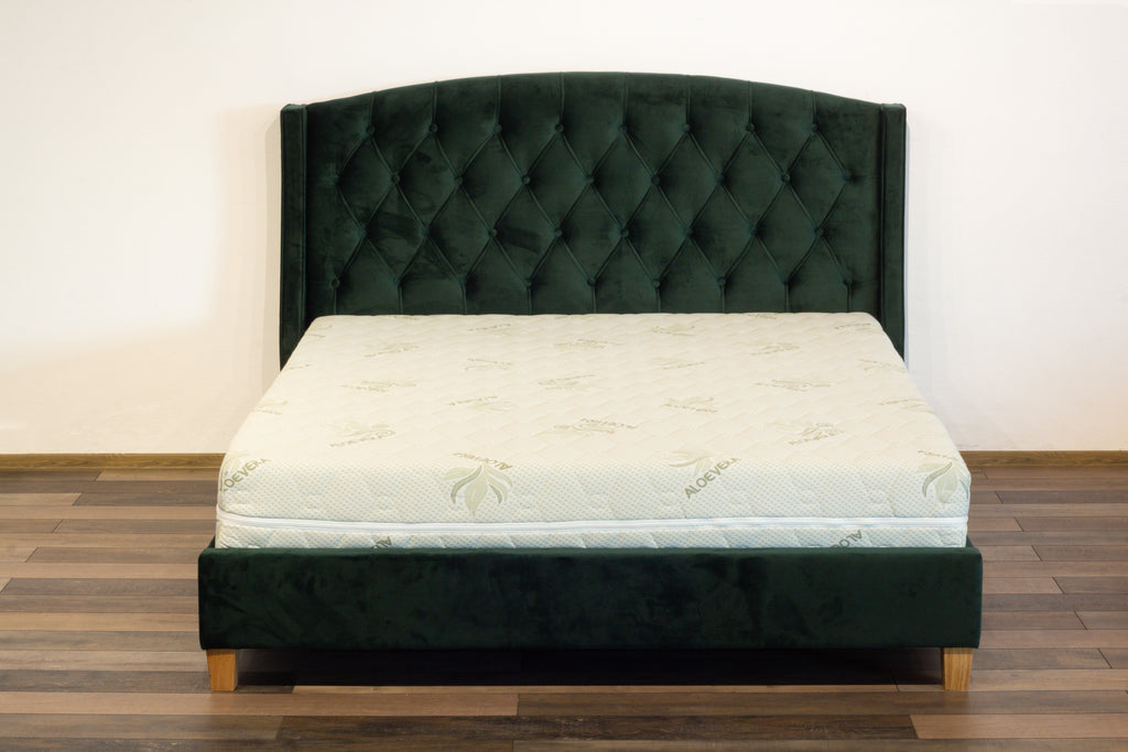 Mattress on a green upholstered bed frame against a white wall.