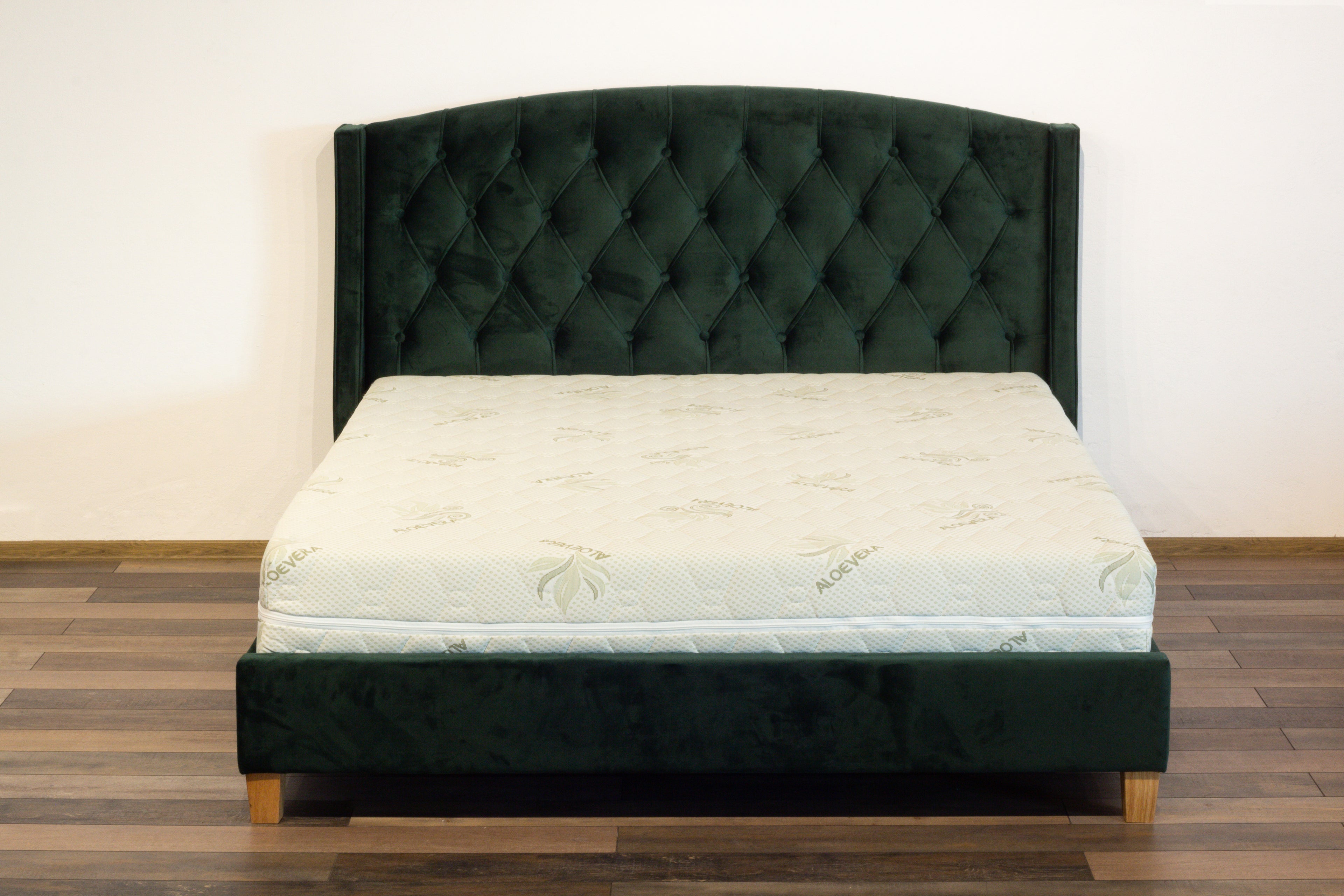Mattress on a green upholstered bed frame against a white wall.