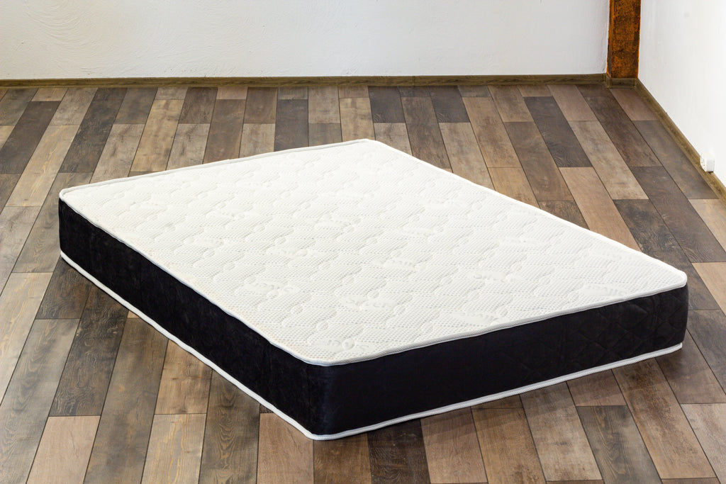 Mattress on a wooden floor with a white wall background