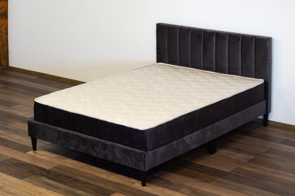 Black upholstered bed frame with beige mattress on a wooden floor.