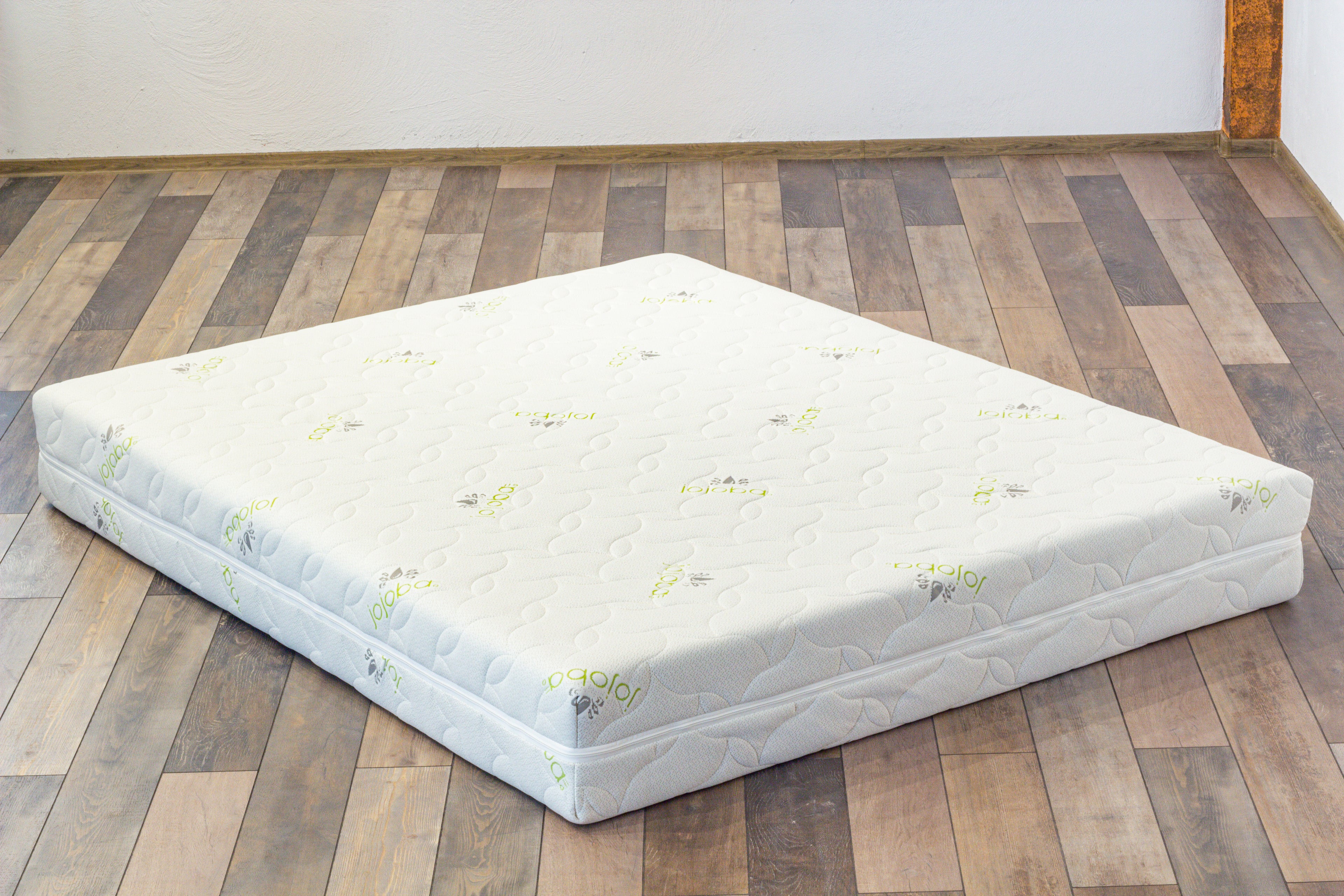 Mattress on a wooden floor with a white wall background